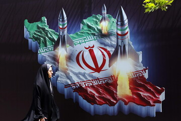 Una donna iraniana accanto a un manifesto contro Israele